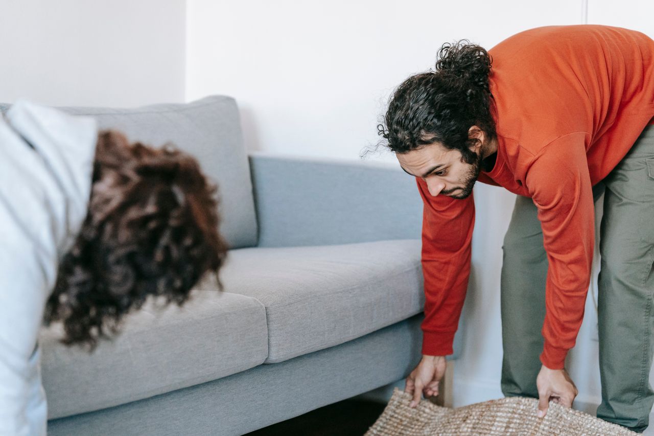Un couple range leur salon, en réorganisant meubles et tapis avec esprit d’équipe.
